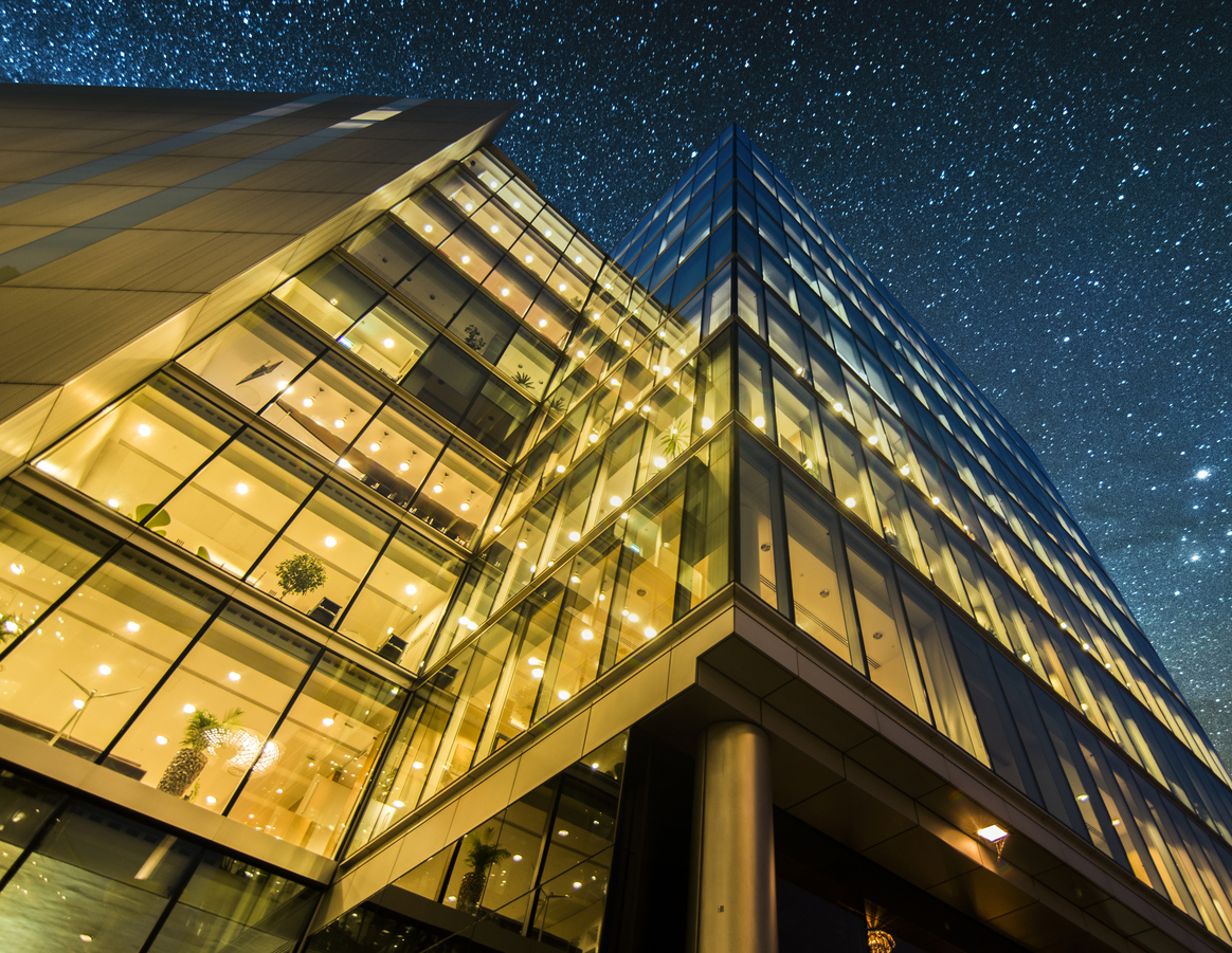 A block of offices at night; perspective is looking up from ground level to the night sky.