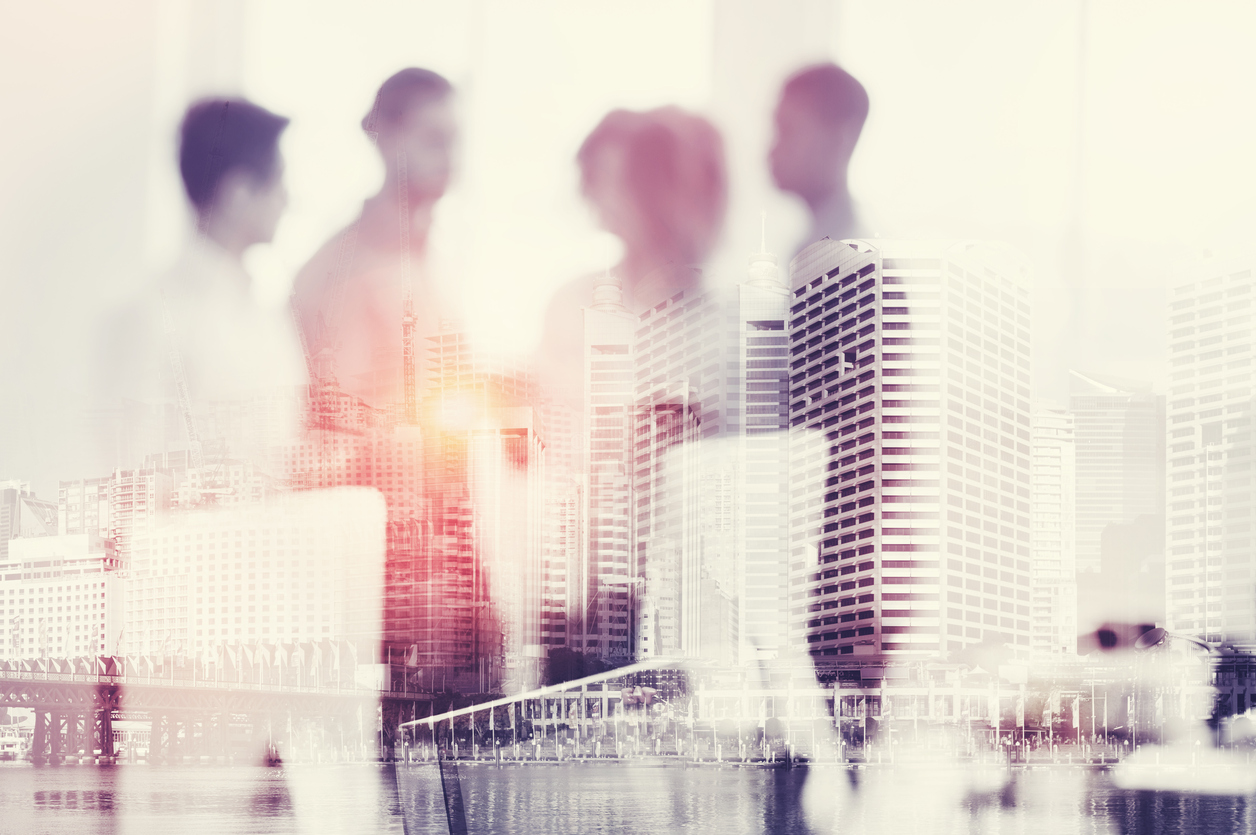 Defocussed group of people working working in an office; buildings are overlayed in the foreground.