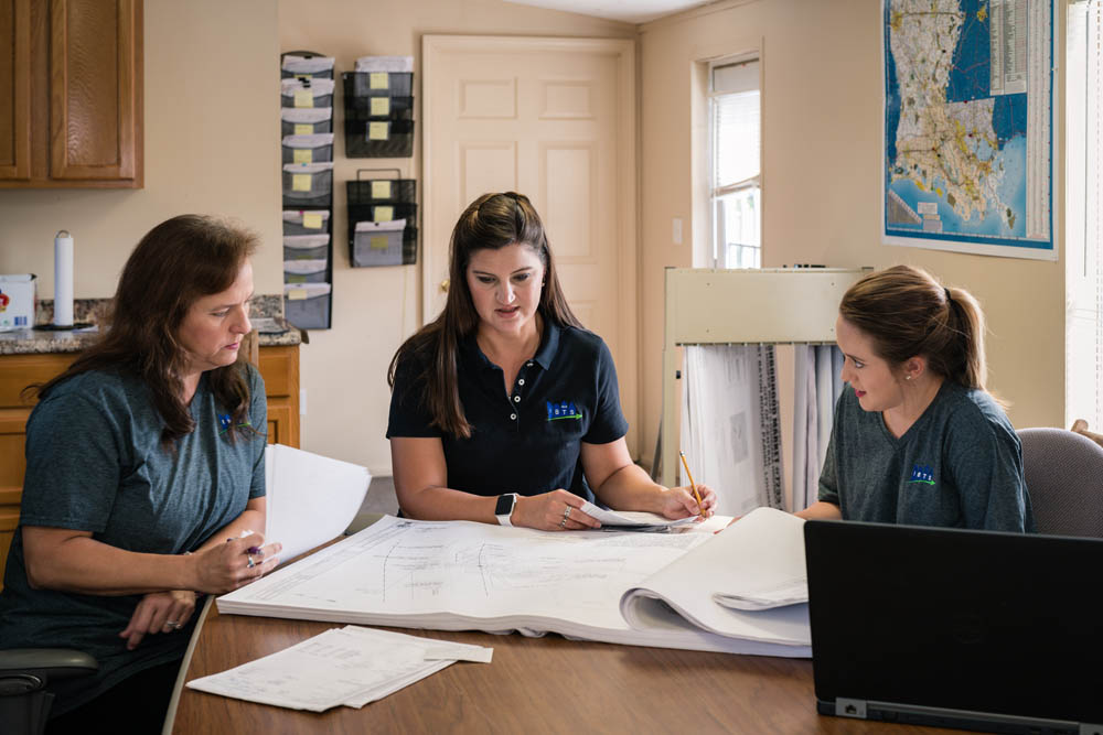Three female IBTS employees examine blueprints around a table for FEMA project.