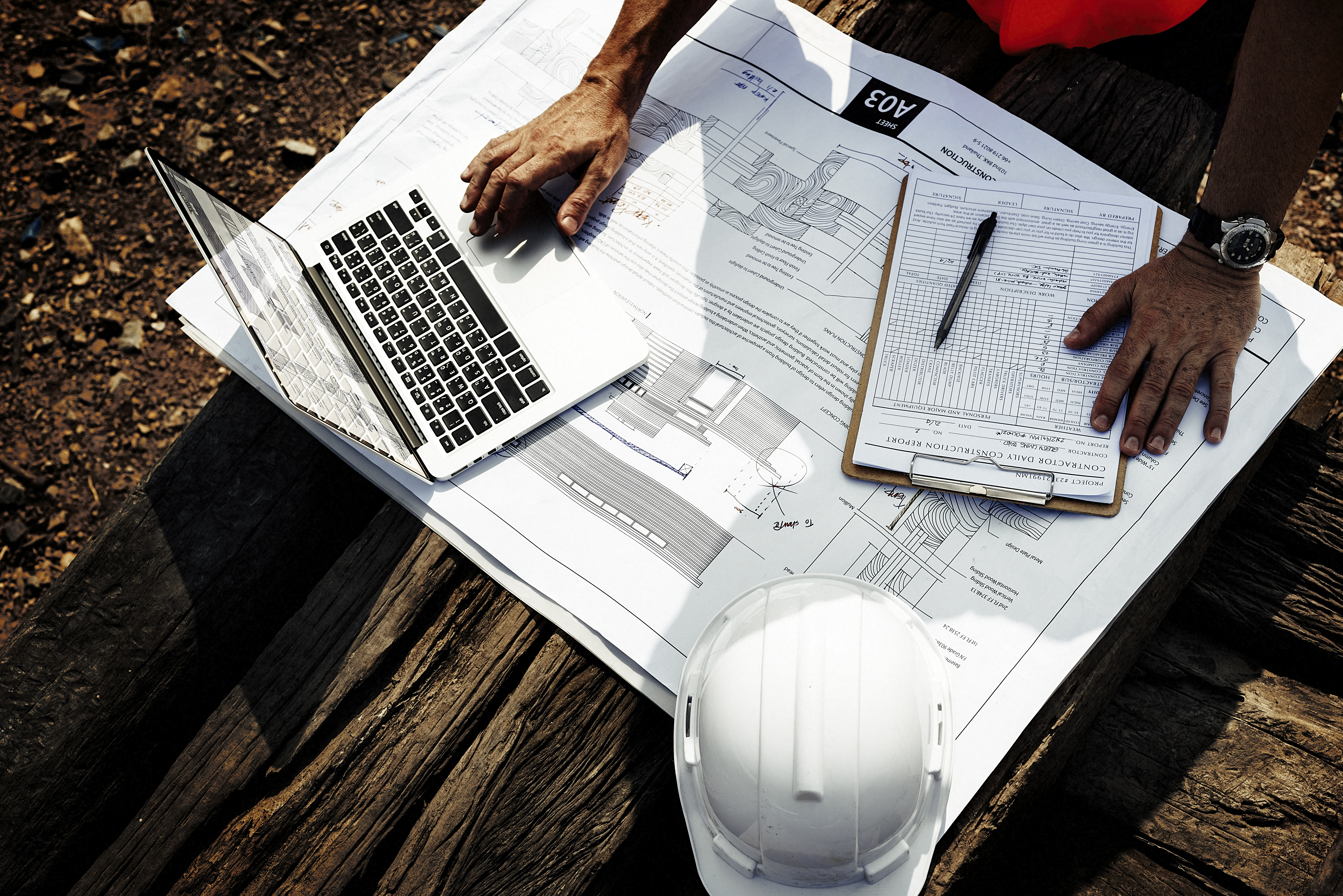 View from above of the hands of a plan reviewer on construction site reviewing printed construction designs.