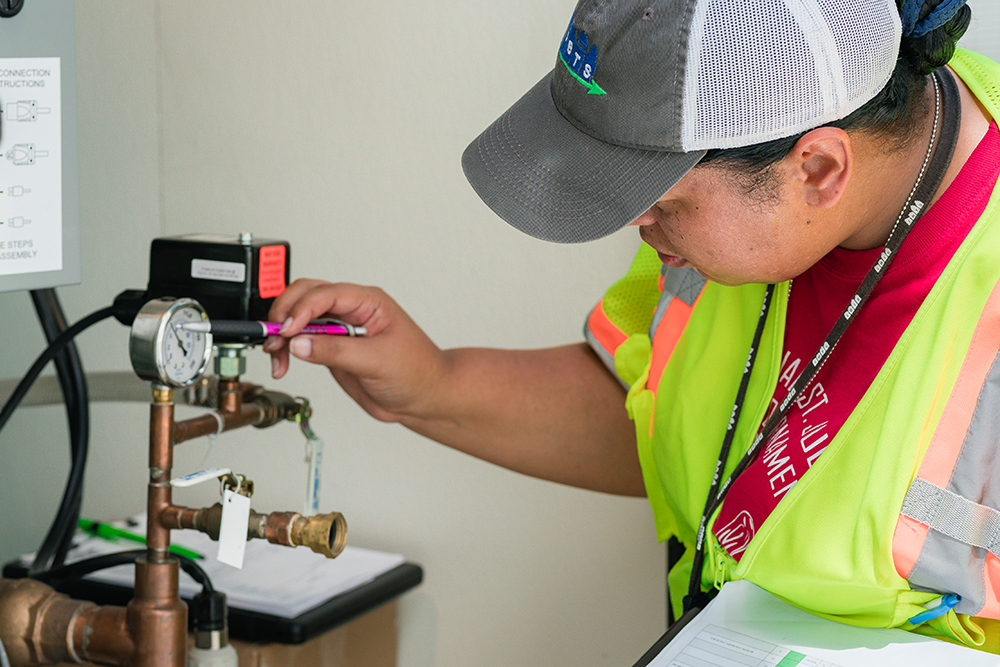 A female IBTS employee holds a clipboard while reading a valve on piping.