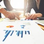 Close up of business man hand pointing at business document on financial paper on wooden desk during discussion at meeting. Group support concept.